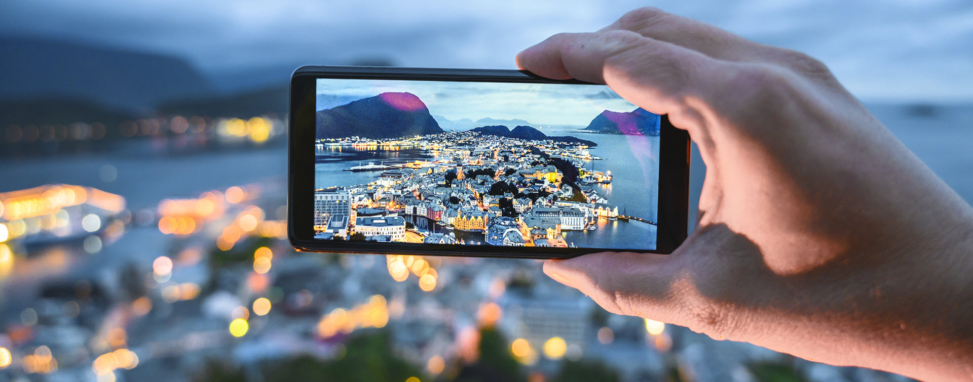 Person holding a smartphone taking a photo of a city at sun down.